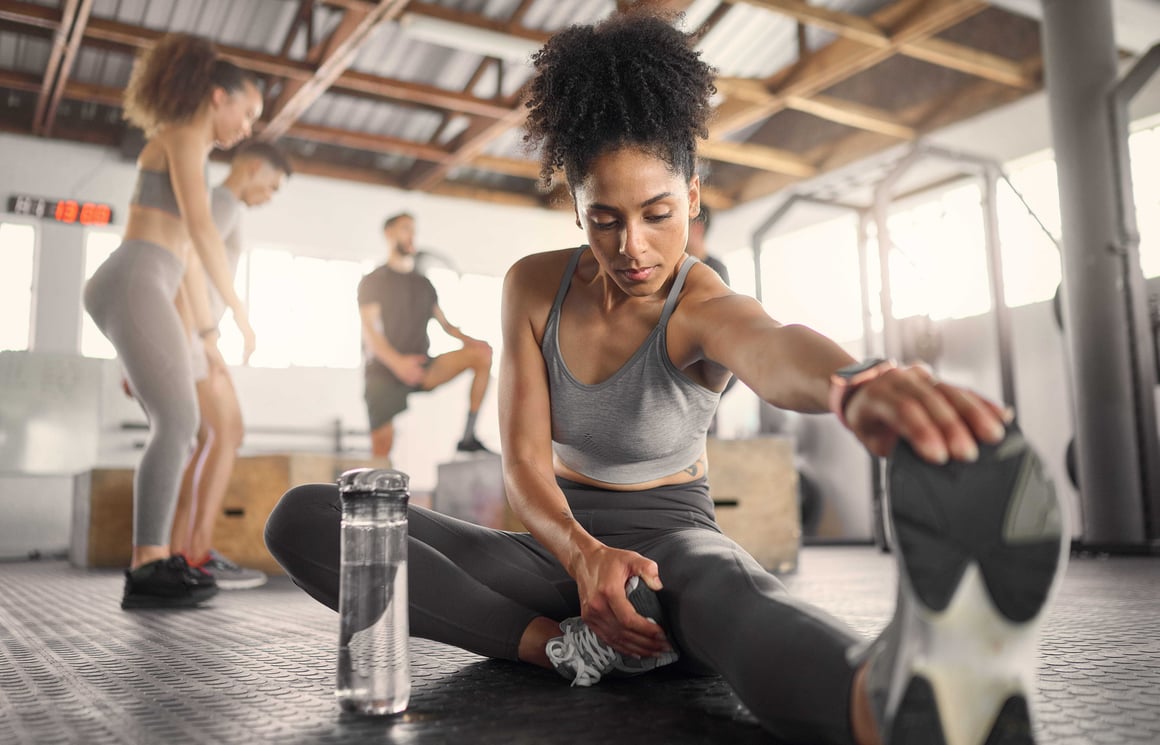 A woman practicing post-workout stretches on a mat in the gym as part of her training routine.